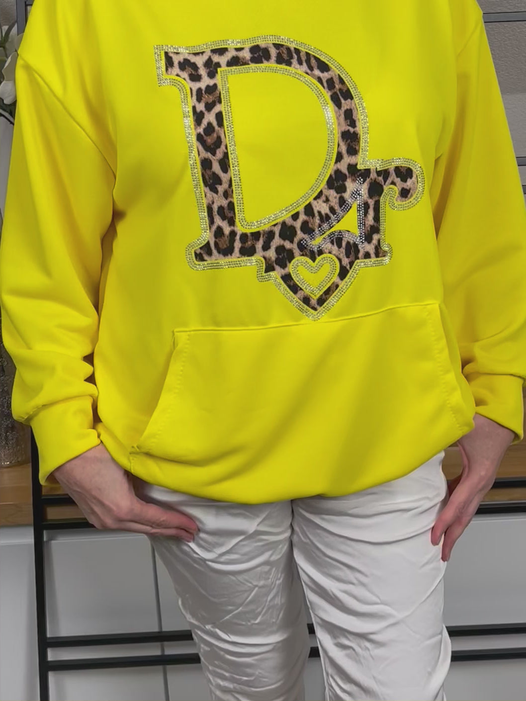 Video eines gelben Hoodies mit Nahaufnahme des auffälligen Animal Print Glitzerdrucks, der im Licht glänzt