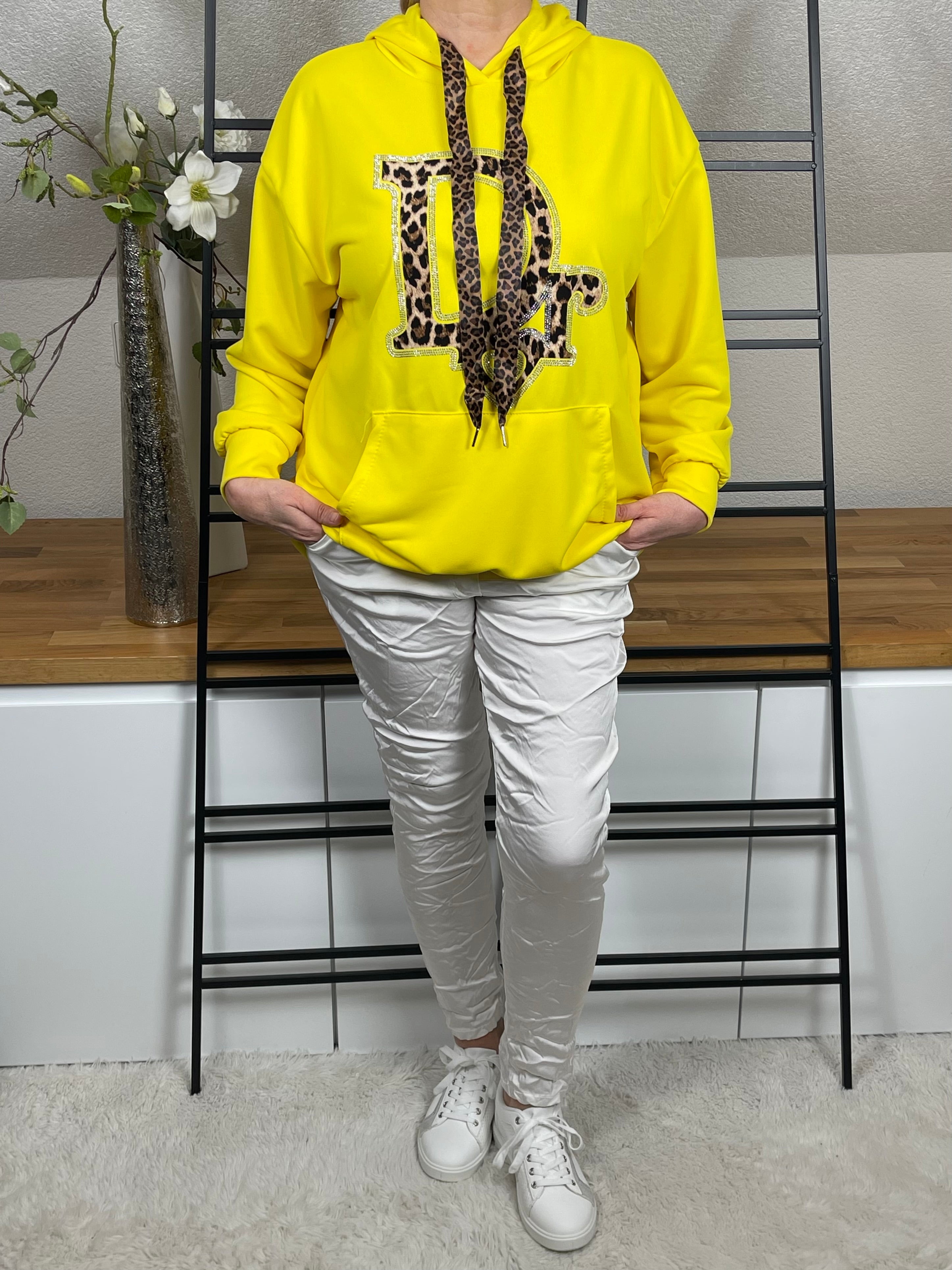 Frontansicht eines gelben Hoodies mit Animal-Print und Glitzerdetails, kombiniert mit weißer Shiney - Hose und Sneakern, geradestehend