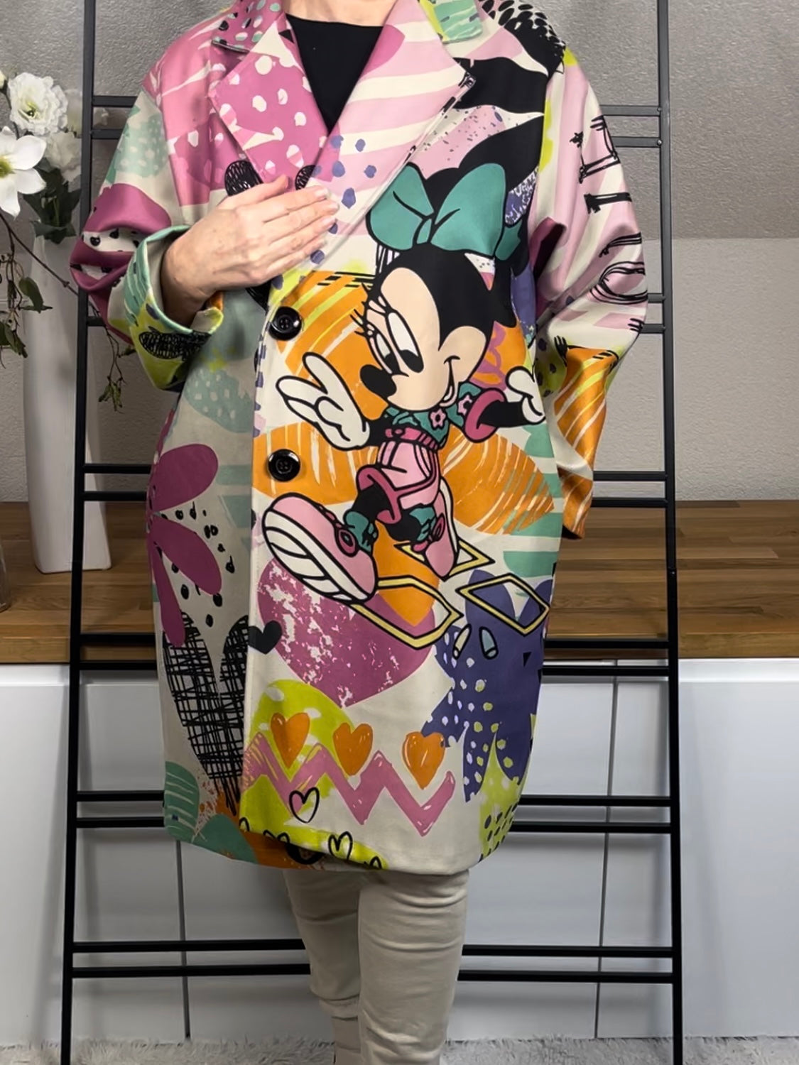 Frontansicht des „Mickey - Mouse“ Oversize-Mantels aus Velour-Optik mit 50 % Wollanteil, deutlich sichtbarem buntem Mickey-Maus-Motiv auf der Vorderseite, praktischen Taschen und schwarzen Knöpfen zum Schließen