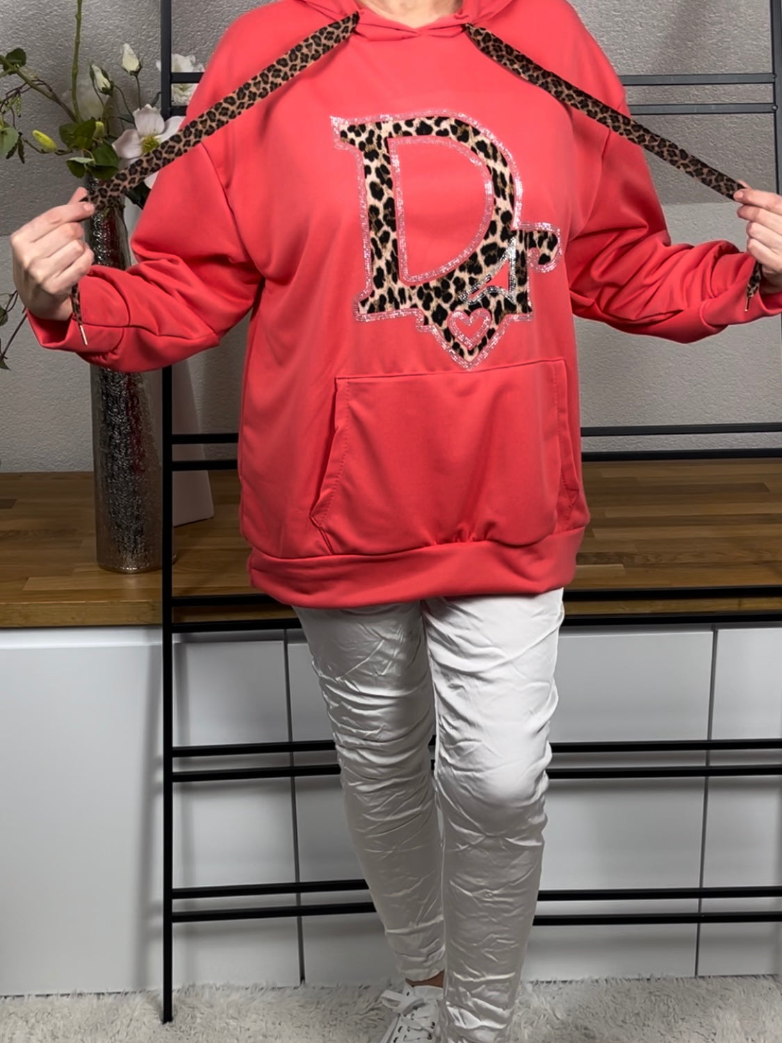 Frontansicht eines korallenen Hoodies mit Glitzer und Animal-Print, Die Kordeln des Hoodies sind nach innen geschlagen , kombiniert mit weißer Shiney - Hose