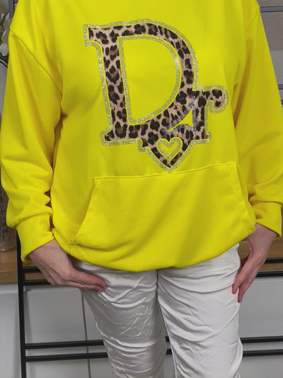 Video eines gelben Hoodies mit Nahaufnahme des auffälligen Animal Print Glitzerdrucks, der im Licht glänzt